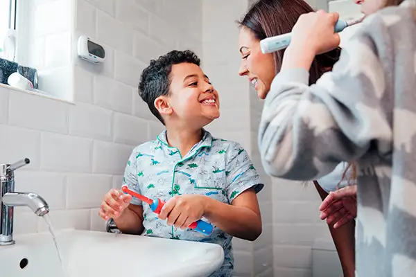 Mother and young son smiling while brushing their teeth together with electric toothbrushes.
