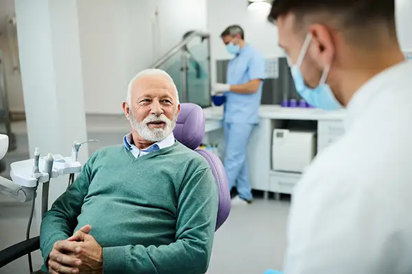 An older male patient sitting in a dental chair and consulting with a dentist in a modern clinic.